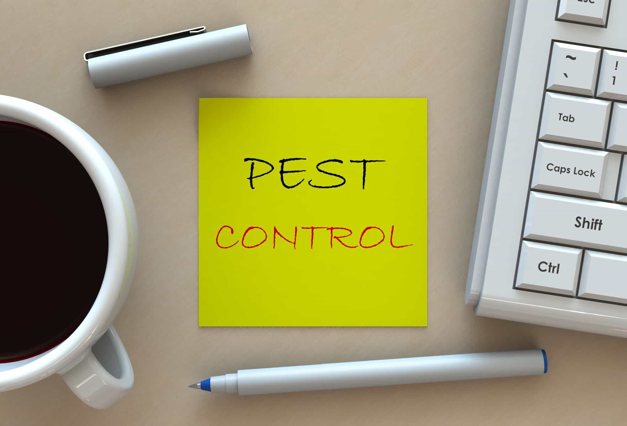 Desk with a coffee cup, keyboard and a sticky note reading pest control