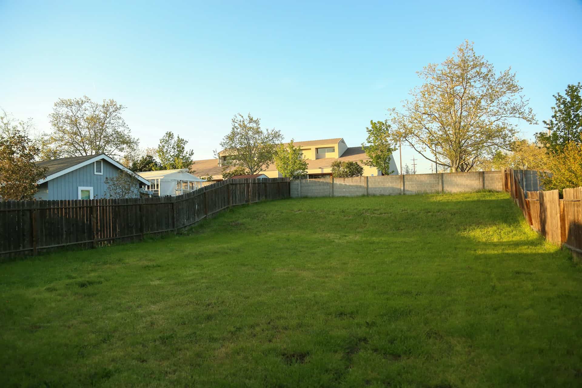 Quiet fenced back yard with open lawn under a clear sky